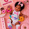 baby, infant, girl, pink, donuts, fluffy_blanket, bow, curly_hair, blocks, milestone, sign, cute, colorful, smiling, playful, soft_toys, celebration, legs, sleeveless_outfit, decorations