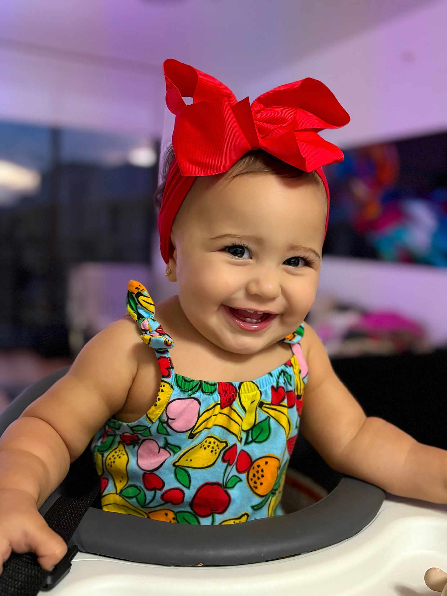 Antonella is registered to the contest to win money with this photo: baby, child, smiling, red_bow, colorful_dress, fruit_pattern, high_chair, indoor, portrait, happy, cute, face, headband, baby_girl, cheerful, infant, person, closeup, sitting, bright