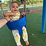 baby, child, swing, playground, green_bow, lemon_pattern, outdoor, happy, smiling, hand_support, blue_swing, feet, infant, park, cute, headband, person, clothing, daylight, grass