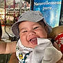 baby, smiling, hat, bib, towel, indoor, market, sign, child, happy, person, closeup, cute, cheerful, portrait, clothing, face, hand, background, expression