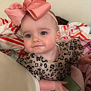 Harmony Fisher joined the competition — help win amazing prizes! baby, child, pink_bow, headband, leopard_print, clothing, blanket, indoor, cute, drool, portrait, sitting, hand, foot, face, expression, young_child, infant, person, soft_lighting