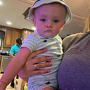 Hudson joined the competition — help win amazing prizes! baby, child, indoor, person, hat, striped_clothing, holding, kitchen, adult_hand, flooring, cabinet, man, cap, wood_floor, casual_clothing, expressionless, furniture, room, portrait, home