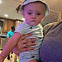 baby, child, indoor, person, hat, striped_clothing, holding, kitchen, adult_hand, flooring, cabinet, man, cap, wood_floor, casual_clothing, expressionless, furniture, room, portrait, home