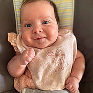 Mia a rejoint le concours — aidez-le/la à gagner de superbes lots ! baby, infant, smile, bib, clothing, face, person, cute, child, soft, cushion, striped, pink, cheeks, eyes, hands, seated, portrait, indoor, trust