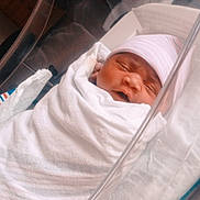 Emyla is registered to the contest to win money with this photo: newborn, baby, blanket, hospital, bassinet, sleeping, infant, wrapped, hat, bed, face, person, cute, soft_lighting, indoor, hospital_room, newborn_care, peaceful, resting, toddler