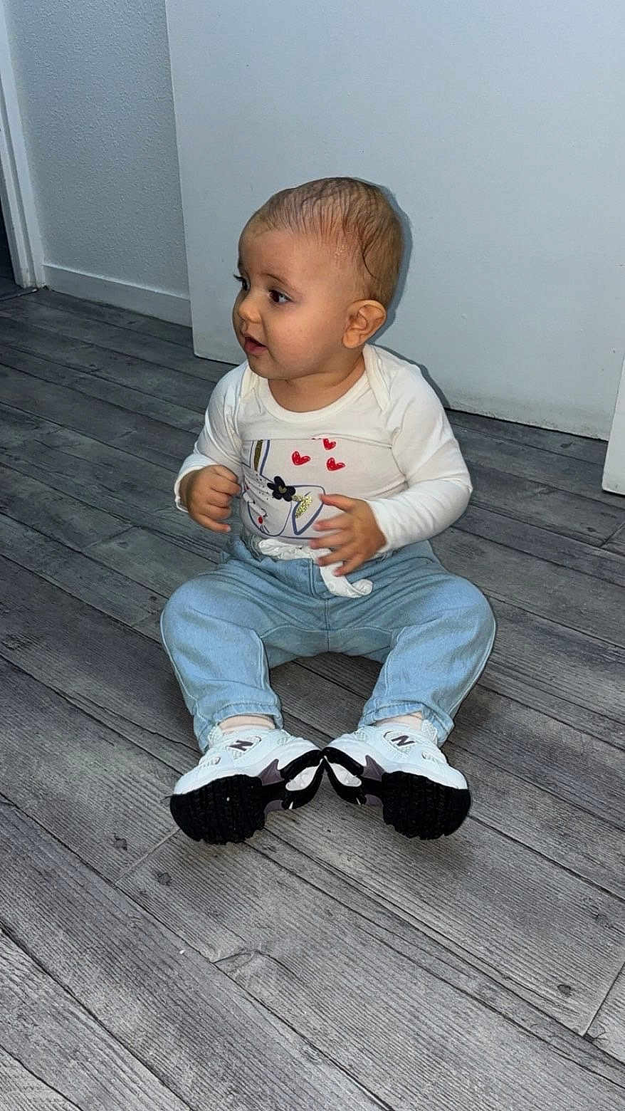 Masha participe au concours pour gagner de l'argent avec cette photo : baby, child, sitting, indoor, floor, wooden_floor, jeans, sneakers, white_shirt, cute, curious, portrait, young_child, casual_clothing, flooring, person, footwear, small_child, toddler, human