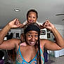 baby, child, woman, smiling, happy, indoor, home, portrait, holding_hands, shoulder_ride, person, furniture, ceiling_fan, braids, headwear, floor_tiles, casual_clothing, joy, family, playful