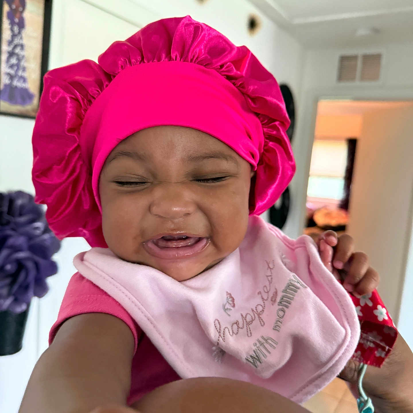 Sareya joined the competition — help win amazing prizes! baby, bib, child, clothing, cute, decor, doorway, expression, face, hand, home, indoor, infant, person, pink_bonnet, pink_shirt, portrait, reaching_hand, smiling, wall_art