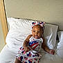 Sareya joined the competition — help win amazing prizes! baby, child, infant, bed, pillow, white_bed_sheet, headband, dress, stars_and_stripes, patriotic, smiling, tongue_out, indoor, furniture, person, cute, happy, skin, sitting, clothing