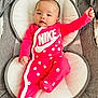 Amara is registered to the contest to win money with this photo: baby, infant, onesie, pink_clothing, nike_logo, smiley_faces, baby_seat, cushion, plush_toys, star_toy, moon_toy, grey_fabric, carpet, portrait, child, cute, relaxed, indoors, face, person