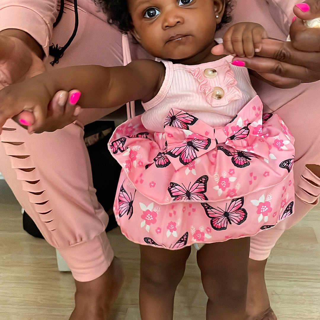 Zyoni joined the competition — help win amazing prizes! adult_hands, baby, butterfly_pattern, child, close_up, curly_hair, cute, foot, holding_hands, indoor, matching_outfit, nail_polish, person, pink_dress, skin, standing, support, toddler, toes, wooden_floor