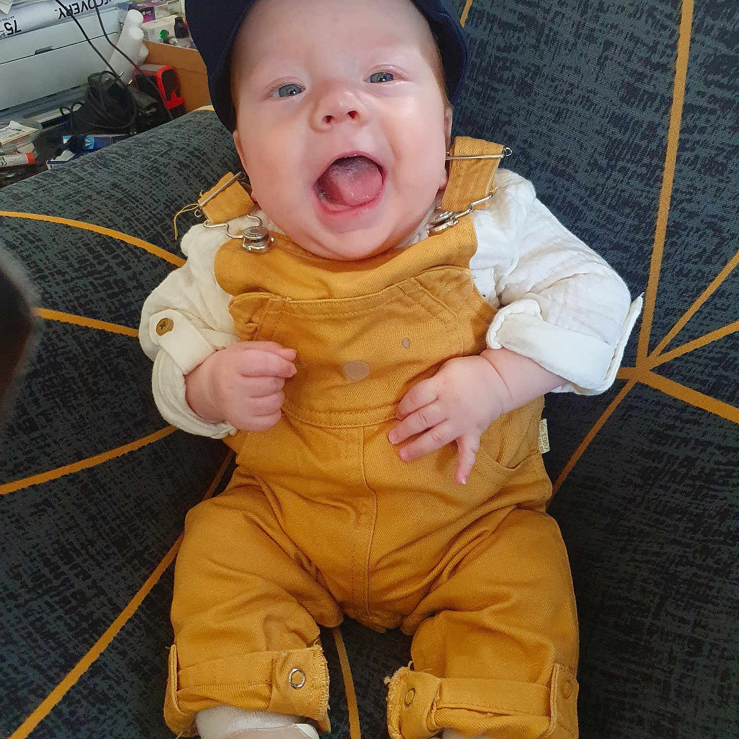 Artan participe au concours pour gagner de l'argent avec cette photo : baby, cap, chair, child, clothing, cute, expression, face, footwear, hands, happy, indoor, infant, joyful, overalls, patterned_chair, person, portrait, sitting, smiling