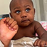 baby, infant, child, portrait, face, eyes, wide_eyed, sitting, indoors, bedroom, blanket, bedding, adult_hand, hand_holding, brown_skin, bare_chest, short_hair, doorway, home, close_up