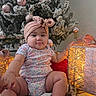 baby, child, infant, portrait, sitting, christmas, christmas_tree, ornaments, gift, present, holiday, festive, headband, bow, floral_clothing, smiling, indoor, cozy, fairy_lights, glowing