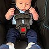 baby, car_seat, infant, child, seatbelt, clothing, footwear, blue_pants, white_shoes, black_car_seat, safety_harness, young_child, indoor, portrait, cute, serious_expression, small_hands, head, face, person