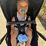 baby, stroller, pacifier, blue_eyes, plush_toy, sunlight, outdoor, child, infant, seatbelt, toy, striped_clothing, barefoot, beads, sitting, comfort, portrait, daylight, nature, relaxation