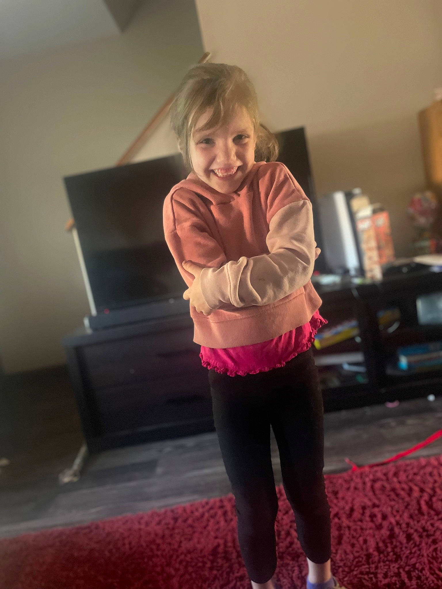 Ava is registered to the contest to win money with this photo: active_pants, blond, comfort, floor, flooring, fun, hardwood, human_leg, joint, joy, knee, long_hair, person, room, shoulder, smile, sportswear, standing, sweatpant, thigh