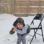 Carlos joined the competition — help win amazing prizes! child, snow, outdoor, winter, peace_sign, smiling, folding_chair, snowfall, fence, clothing, boots, playful, young, happy, casual, person, nature, cold, daytime, fun