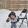 child, snow, outdoor, winter, peace_sign, smiling, folding_chair, snowfall, fence, clothing, boots, playful, young, happy, casual, person, nature, cold, daytime, fun