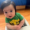 Santino joined the competition — help win amazing prizes! baby, child, infant, face, person, green_shirt, cartoon_character, high_chair, indoor, wooden_floor, bedspread, blue, curly_hair, cute, smiling, looking_up, soft_focus, portrait, playful, happy