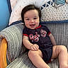 baby, child, smile, happy, sitting, cushion, chair, clothing, red_sox, infant, face, cute, indoor, blanket, pattern, wood, person, portrait, baby_blanket, comfort
