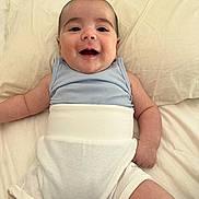 Isaac participe au concours pour gagner de l'argent avec cette photo : baby, smiling, infant, bed, clothing, blue_top, white_bottoms, happy, cute, lying_down, skin, head, arms, legs, indoors, soft_surface, face, portrait, child, toddler