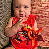 baby, cartoon_car, child, couch, cushion, eyes, fabric, face, hands, home, indoor, infant, photography, portrait, racing_shirt, red_clothing, serious_expression, sitting, toy, toy_steering_wheel