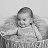 Easton Hanrahn is registered to the contest to win money with this photo: baby, basket, blanket, black_and_white, child, cute, expression, face, furniture, infant, indoors, knitted_clothing, looking_away, person, portrait, smile, soft_texture, sitting, young_child, woven