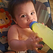 Juan Carlos joined the competition — help win amazing prizes! baby, infant, child, bottle, feeding, drinking, seated, highchair, portrait, face, eyes, hands, arms, legs, blanket, colorful, indoor, close_up, baby_seat, adorable