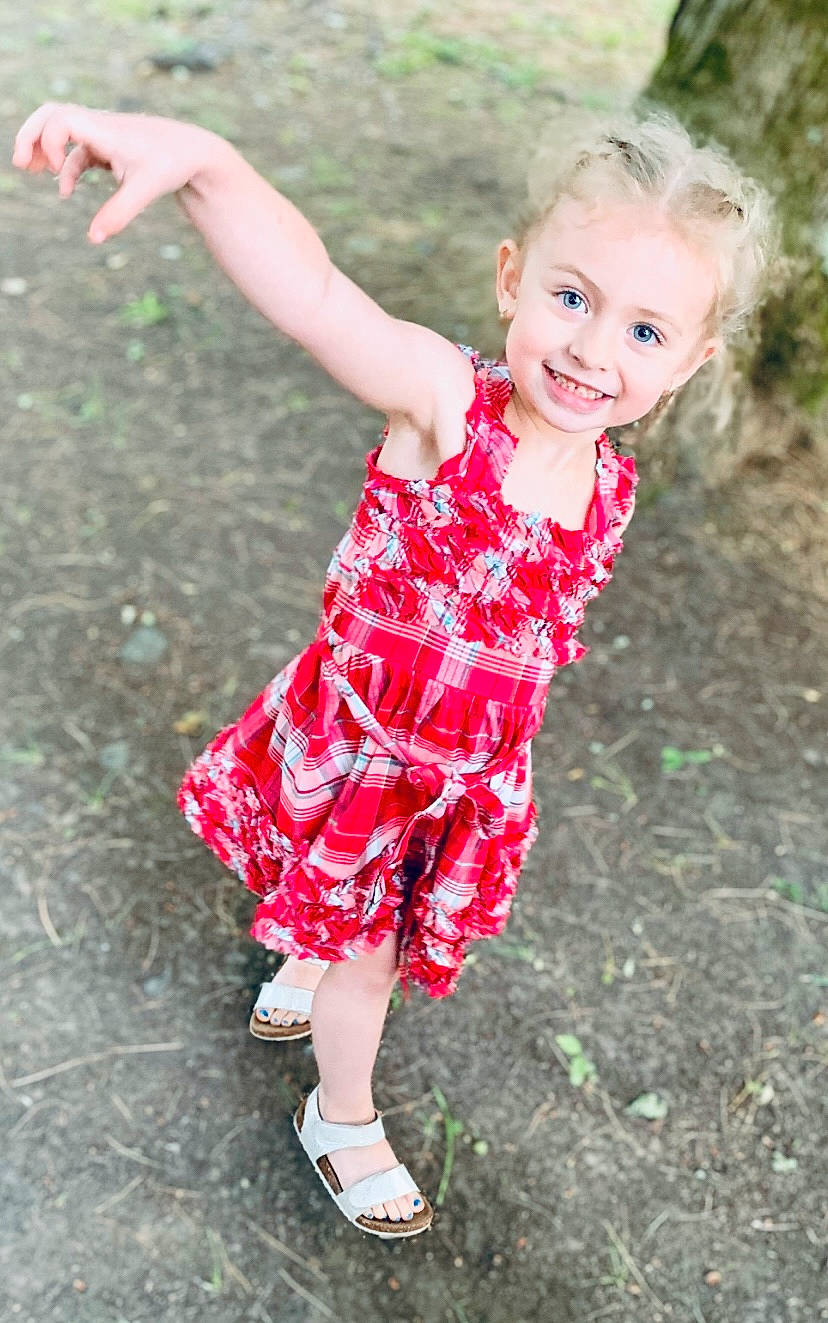 Layla is registered to the contest to win money with this photo: baby_toddler_clothing, day_dress, dress, face, flash_photography, fun, gesture, grass, happy, human_leg, joy, pattern, people_in_nature, person, pink, plant, sandal, skin, smile, summer