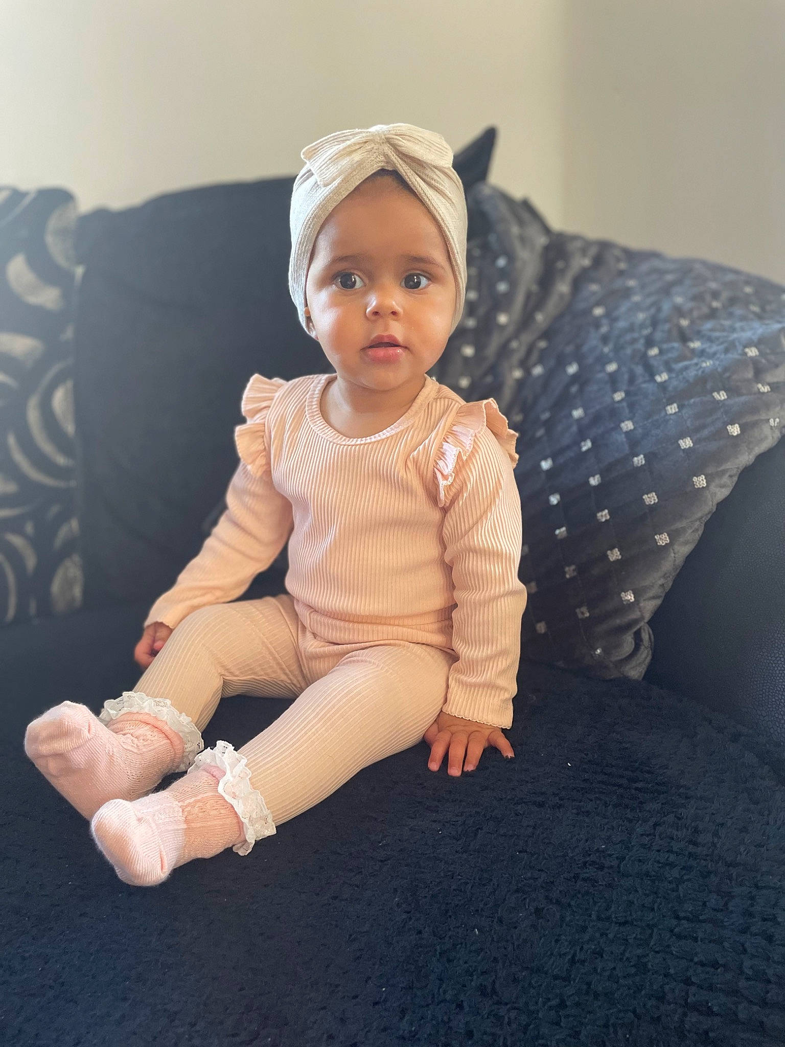 Giana is registered to the contest to win money with this photo: baby, baby_toddler_clothing, barefoot, child, comfort, elbow, eye, fashion_accessory, flooring, foot, happy, headwear, human_leg, knee, linens, pattern, person, sitting, sleeve, thigh