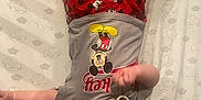 Oliver is registered to the contest to win money with this photo: baby, blanket, blue_eyes, child, clothing, cute, elephant_pattern, face, foot, hand, hat, headwear, indoors, infant, lying_down, mickey_mouse, pacifier, person, shirt, shorts