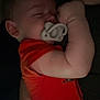 baby, sleeping, pacifier, orange_clothing, infant, arm, hand, closeup, cuddle, person, skin, rest, peaceful, indoor, dark, comfort, parent, child, face, relaxation