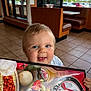 Kaiden is registered to the contest to win money with this photo: baby, child, menu, restaurant, indoor, smiling, blue_eyes, food, pizza, pasta, table, tile_floor, window, daylight, person, cute, happy, hand, clothing, diner