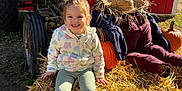Kenzie is registered to the contest to win money with this photo: child, girl, smiling, hay_bale, tractor, pumpkin, scarecrow, straw_hat, outdoor, farm, fall, autumn, sunlight, clothing, footwear, nature, ground, agriculture, person, rural