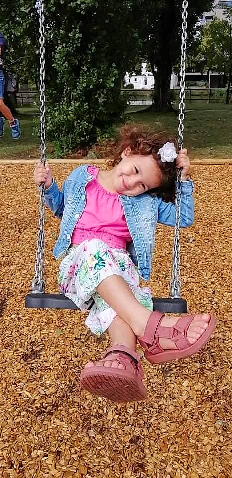 Naëlle a rejoint le concours — aidez-le/la à gagner de superbes lots ! blue, facial_expression, grass, green, hand, joy, leg, leisure, mammal, nature, people_in_nature, person, playground, product, public_space, recreation, swing, toddler, tree, vertebrate