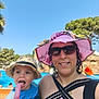 child, woman, pool, summer, hat, sunglasses, popsicle, smile, outdoor, water_slide, trees, blue_sky, vacation, sunhat, swimsuit, holiday, playful, family, fun, sunshine