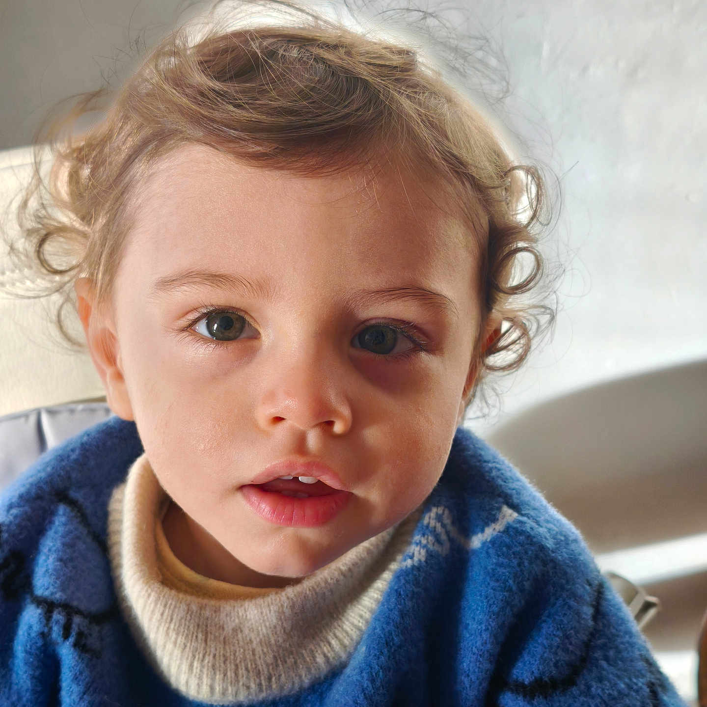 Adam Aaron Cooper participe au concours pour gagner de l'argent avec cette photo : baby, blue_sweater, casual_clothing, child, closeup, cozy, curiosity, curly_hair, cute, expression, eyes, face, indoors, natural_light, person, portrait, smiling, soft_light, toddler, young_child