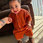 Jaime joined the competition — help win amazing prizes! baby, child, infant, orange_clothing, knitwear, smile, drool, standing, hand_holding, brown_shoes, carpet, sunlight, vertical_blinds, indoor, couch, happy, person, portrait, cute, toddler