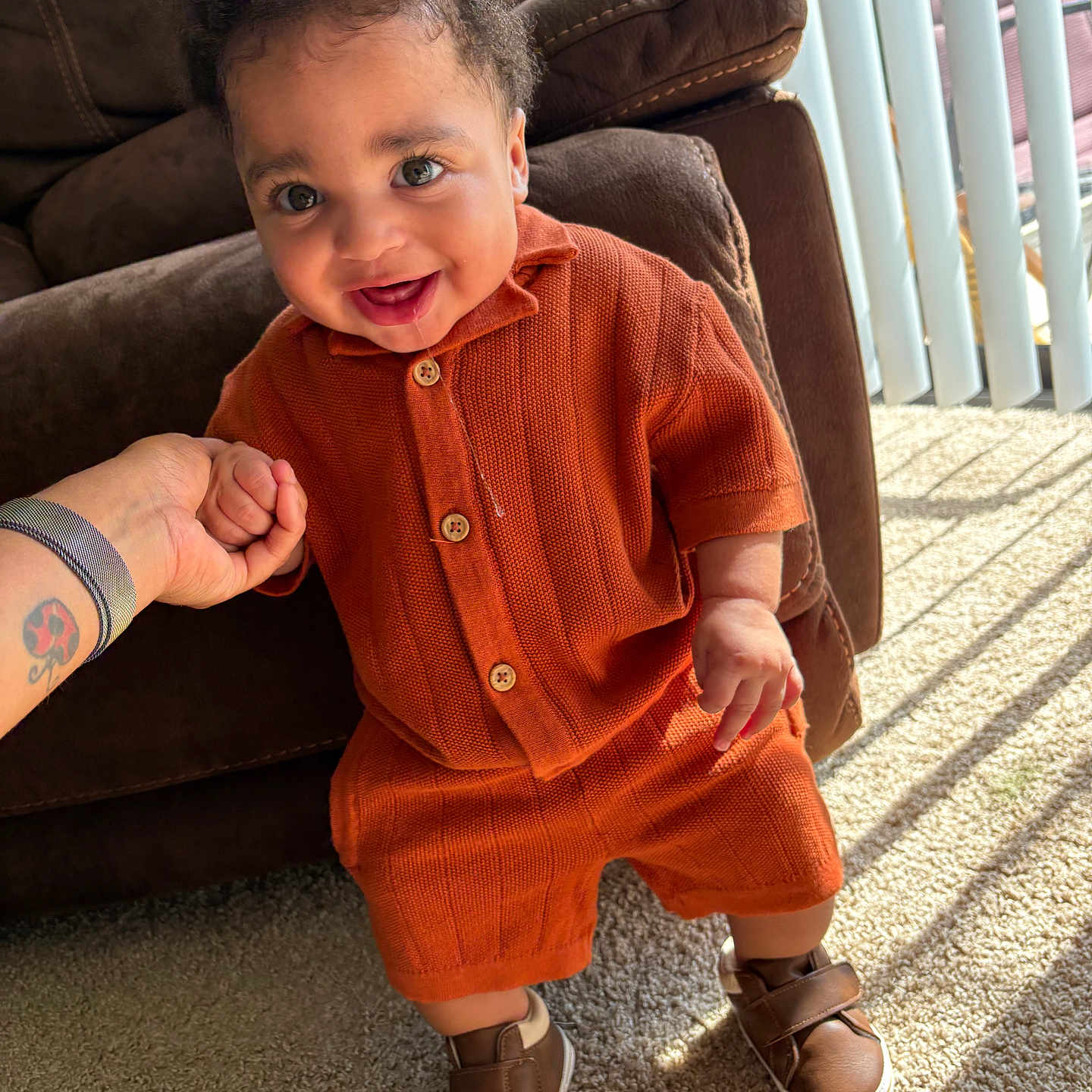 Jaime joined the competition — help win amazing prizes! baby, child, infant, orange_clothing, knitwear, smile, drool, standing, hand_holding, brown_shoes, carpet, sunlight, vertical_blinds, indoor, couch, happy, person, portrait, cute, toddler