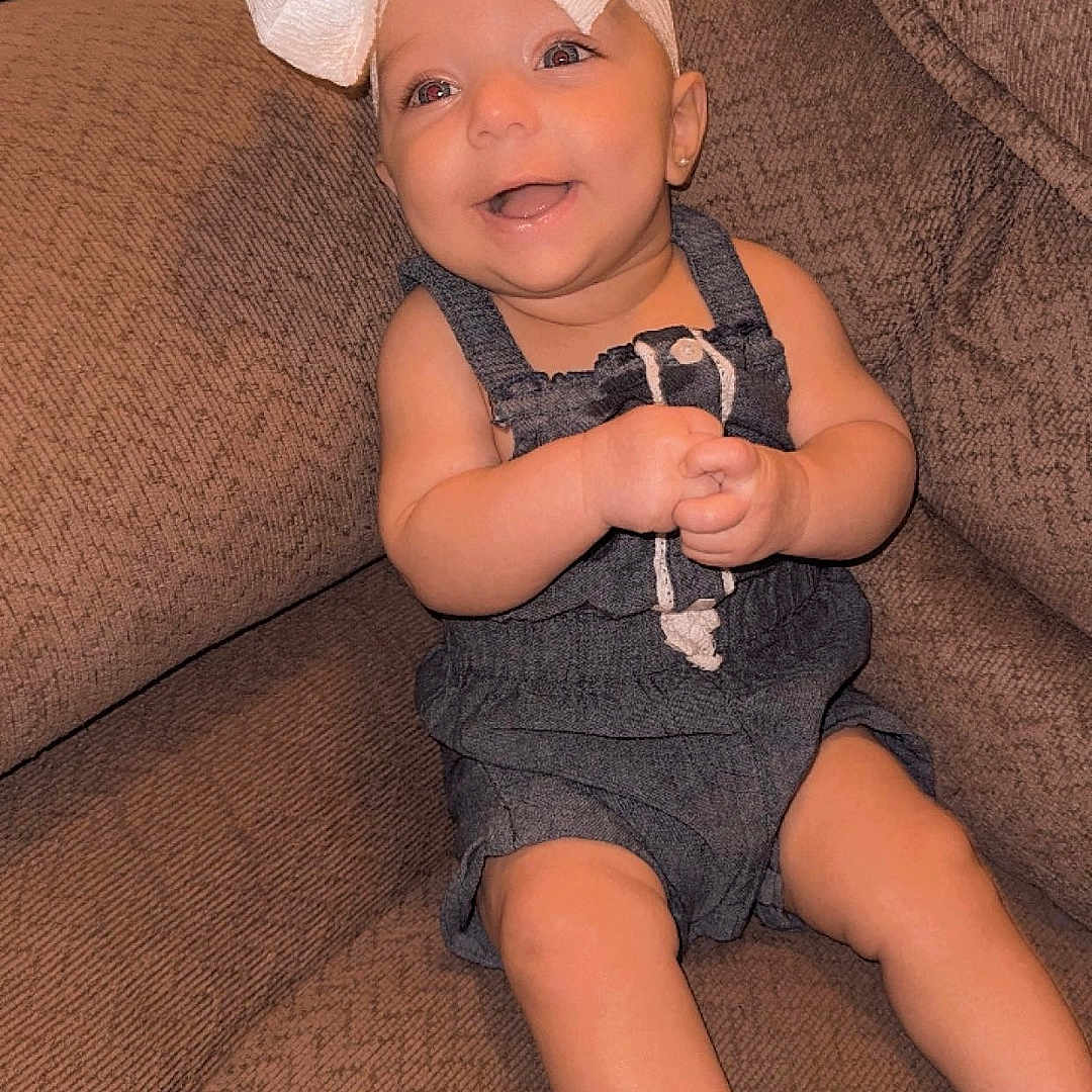 Kelly is registered to the contest to win money with this photo: baby, barefoot, bow, child, clothing, couch, cute, denim, expression, furniture, happy, headwear, indoors, infant, person, portrait, sitting, skin, smiling, young