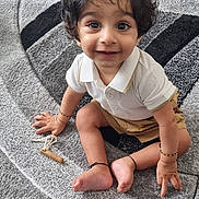Viaan joined the competition — help win amazing prizes! child, toddler, curly_hair, smiling, sitting, carpet, toy, playroom, indoors, white_shirt, shorts, barefoot, bracelet, floor, happy, cute, young_child, expression, person, home