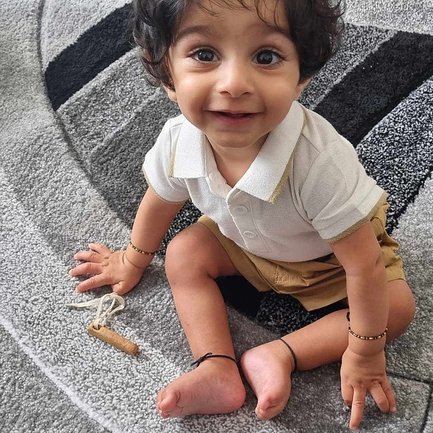 Viaan joined the competition — help win amazing prizes! barefoot, bracelet, carpet, child, curly_hair, cute, expression, floor, happy, home, indoors, person, playroom, shorts, sitting, smiling, toddler, toy, white_shirt, young_child