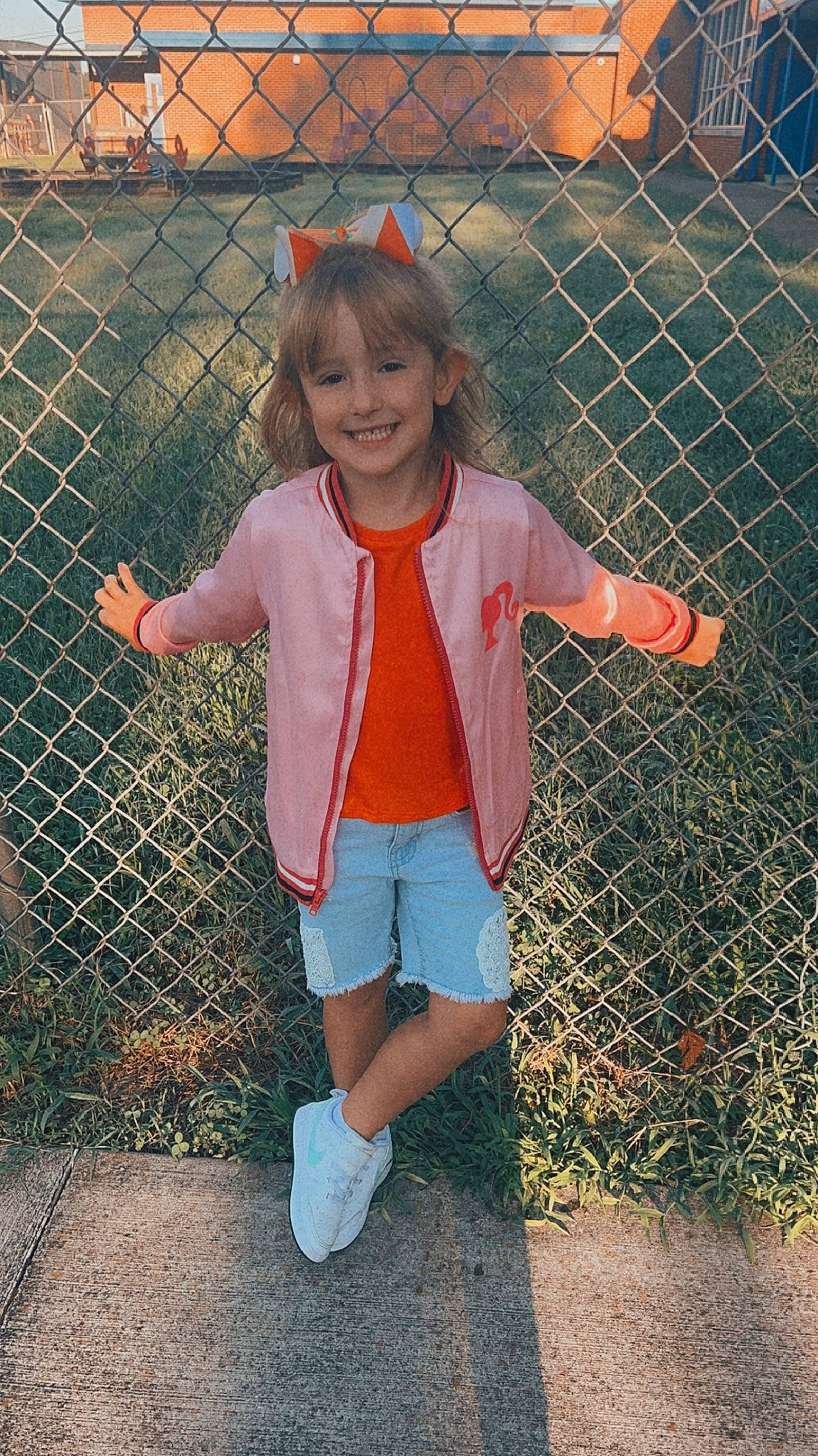 Nila is registered to the contest to win money with this photo: fence, fun, grass, happy, human_leg, joy, leisure, mesh, people_in_nature, person, pink, plant, product, shorts, sleeve, smile, standing, thigh, toddler, tree