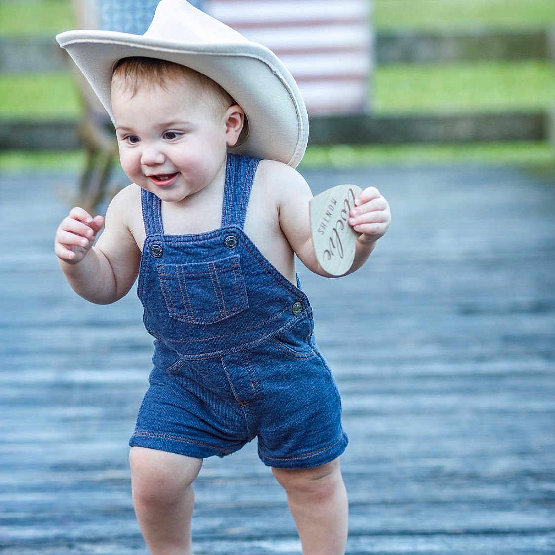 Lanceton joined the competition — help win amazing prizes! toddler, child, denim_overalls, cowboy_hat, barefoot, outdoor, wooden_deck, american_flag, milestone_card, happy, smiling, walking, baby, summer, cute, portrait, grass, background_blur, playful, person