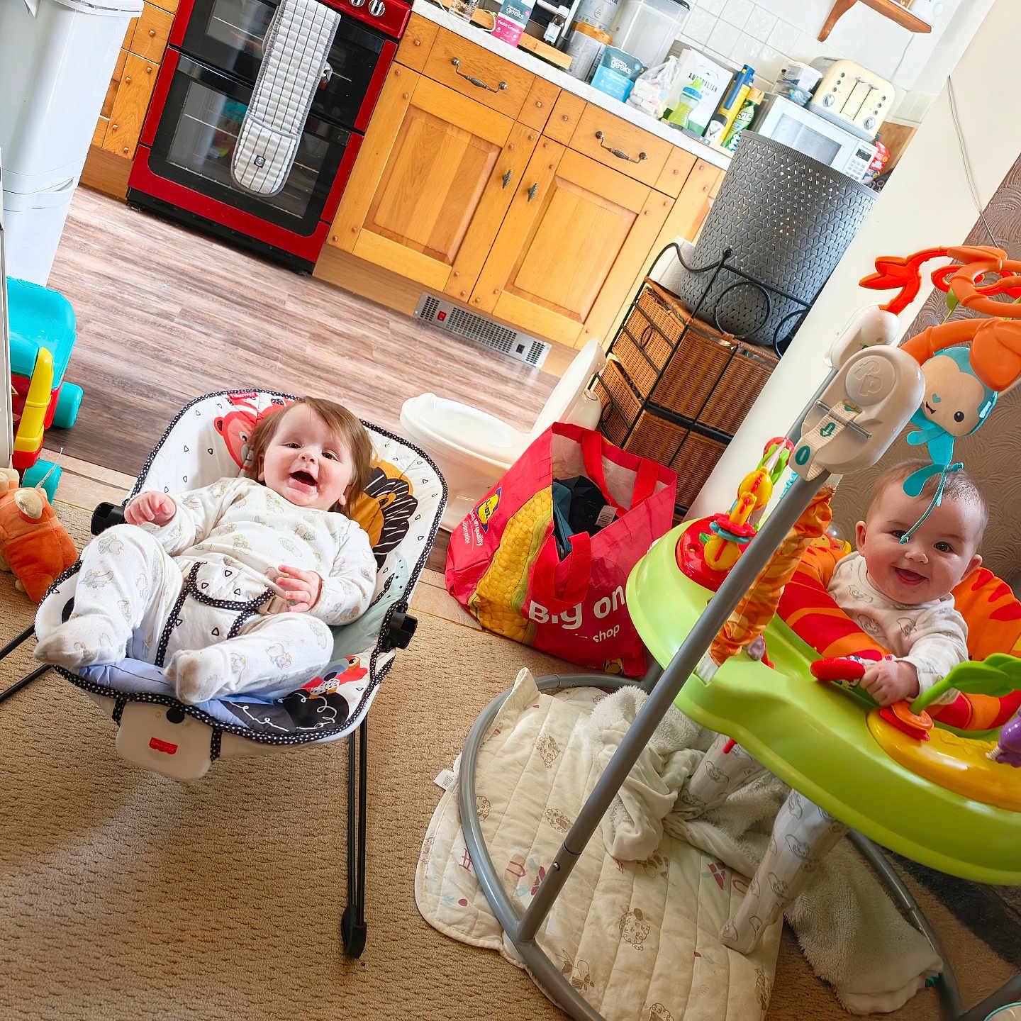 Lola And Jorja joined the competition — help win amazing prizes! baby, babies, child, infant, baby_rocker, activity_jumper, toys, mirror, kitchen, wooden_cabinets, flooring, carpet, smile, happy, play, indoor, furniture, bag, blanket, person