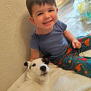 Theo joined the competition — help win amazing prizes! toddler, child, dog, smiling, sitting, blanket, indoor, flooring, wall, clothing, dinosaur_print, pet, happy, furniture, portrait, cute, cozy, young_child, animal, person
