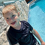Nolan joined the competition — help win amazing prizes! child, boy, smiling, pool, water, swimwear, dinosaur, shorts, black_shirt, stone_wall, sunlight, outdoor, summer, happy, wet_hair, blue_sky, trees, playful, leisure, vacation
