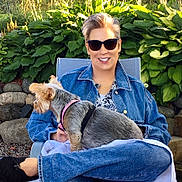 Riley Orouke is registered to the contest to win money with this photo: blue_jeans, canine, casual, chair, denim_jacket, dog, earrings, footwear, garden, greenery, happy, leafy_plants, outdoor, person, pet, relaxing, short_hair, smiling, stone_wall, sunglasses