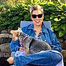 blue_jeans, canine, casual, chair, denim_jacket, dog, earrings, footwear, garden, greenery, happy, leafy_plants, outdoor, person, pet, relaxing, short_hair, smiling, stone_wall, sunglasses